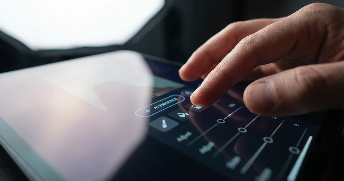 Detail rukou upravujících fotografii na tabletu pomocí umělé inteligence.
