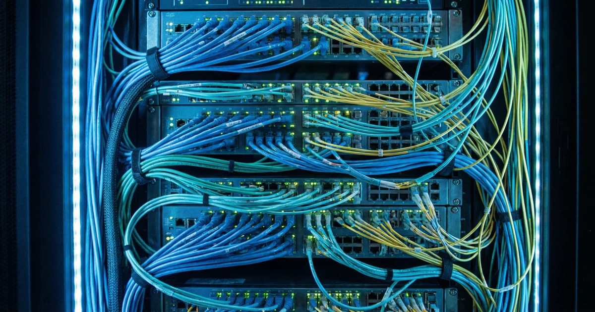 Detailní záběr na propletené síťové kabely a blikající kontrolky v serverovně, symbolizující blockchain.