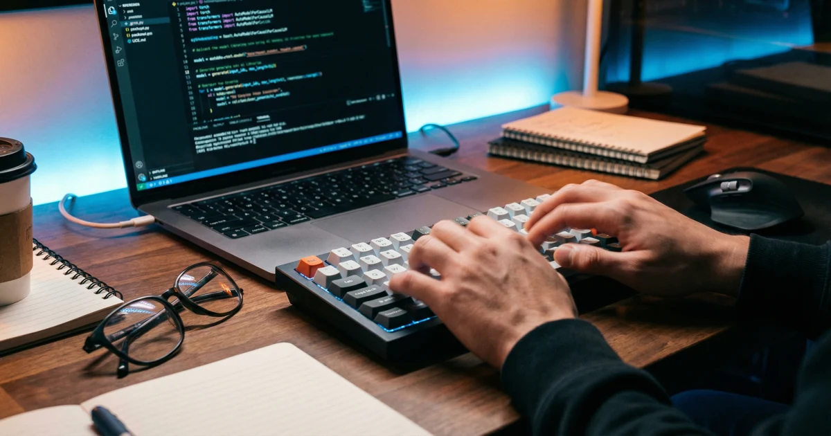 Detailní záběr rukou píšících na klávesnici s odrazem Python kódu na obrazovce.